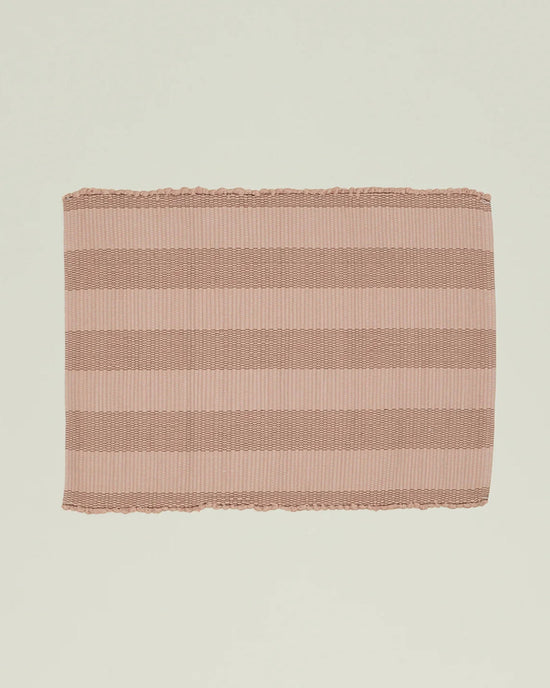 The Essential Floor Mat in Blush by Hawkins New York is a rectangular, ribbed mat with wide light pink and brown stripes, crafted from recycled fibers.