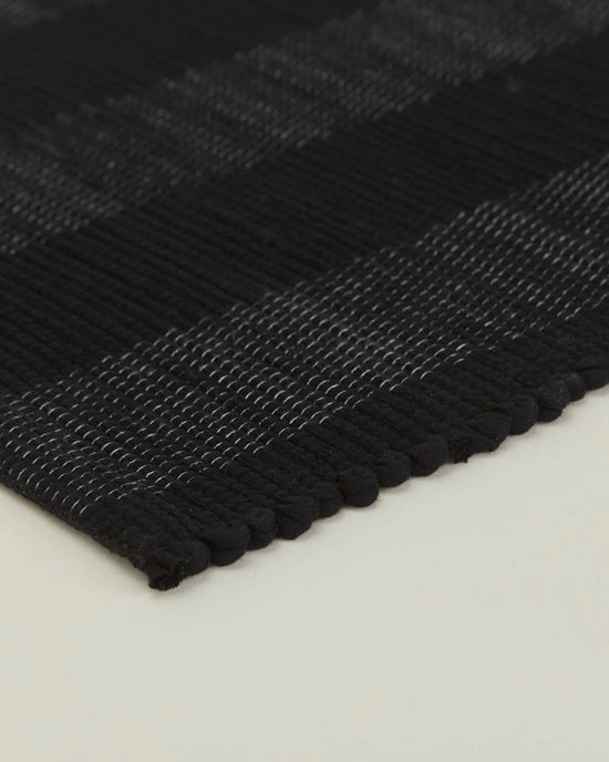 Close-up of the corner of the Essential Floor Runner in Black by Hawkins New York, crafted from recycled fibers and placed on a light-colored surface.