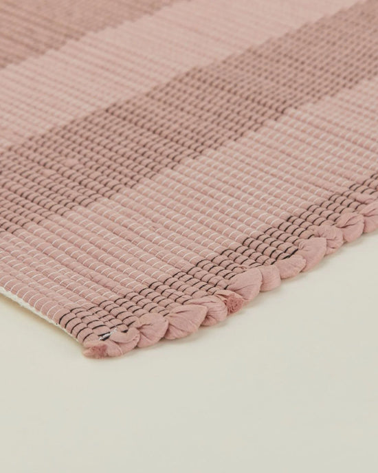 Close-up of the Hawkins New York Essential Floor Runner in Blush, featuring pink and beige stripes with braided edging, crafted from recycled fibers and displayed on a light surface.