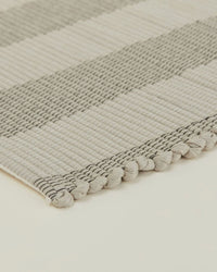 Close-up of the Hawkins New York Essential Floor Runner in Light Grey, machine washable with alternating light and dark stripes and a textured, knotted edge shown on a neutral background.