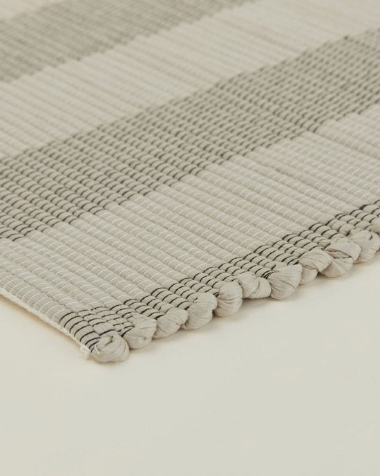 Close-up of the Hawkins New York Essential Floor Runner in Light Grey, machine washable with alternating light and dark stripes and a textured, knotted edge shown on a neutral background.