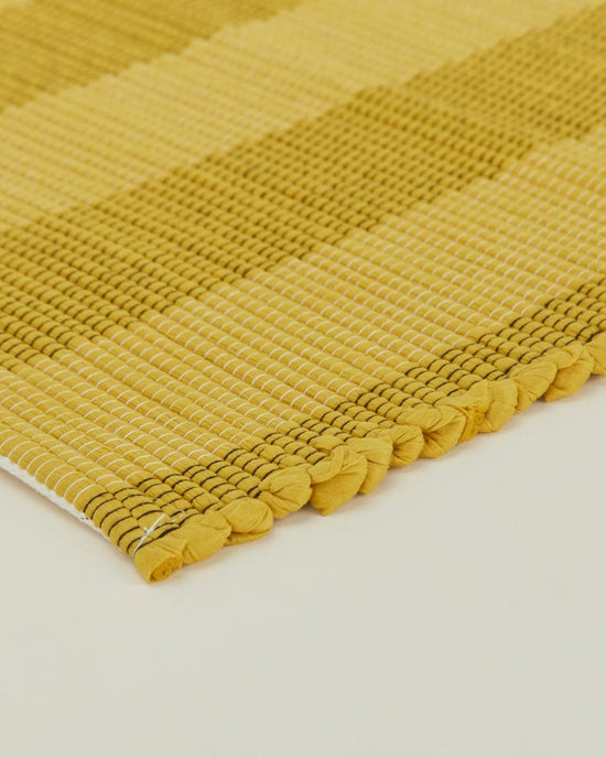 Close-up of the Essential Floor Runner in Mustard by Hawkins New York, showing its hand loomed checkered texture and knotted ends on a light surface—perfect as a floor runner and conveniently machine washable.