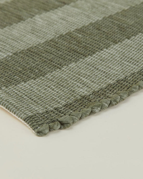 Close-up of the Essential Floor Runner in Olive by Hawkins New York, featuring a green and white checkered pattern, textured recycled fibers, and finished edge displayed on a light surface.