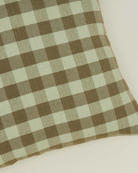 A close-up of the Hawkins New York Essential Gingham Pillow, 18x18 inches in sage/olive, featuring a machine washable checkered pattern on a light background.