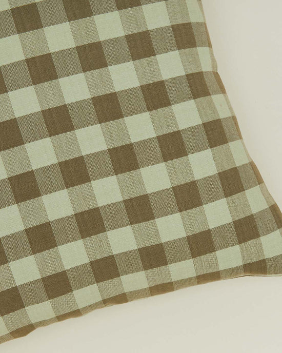 A close-up of the Hawkins New York Essential Gingham Pillow, 18x18 inches in sage/olive, featuring a machine washable checkered pattern on a light background.