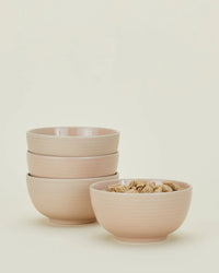 Four blush Essential Large Bowls by Hawkins New York are shown—three stacked, one filled with cereal against a plain background. This set of dishwasher-safe stoneware bowls offers easy cleanup and stylish versatility.