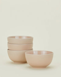 Four blush Essential Large Bowls by Hawkins New York are stacked—three in a stack and one in front—against a plain light background. This set of stoneware bowls is dishwasher safe, combining everyday convenience with style.