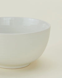 A close-up of a Hawkins New York Essential Large Bowl in Bone, from their stoneware dinnerware set of 4, displayed against a light beige background.