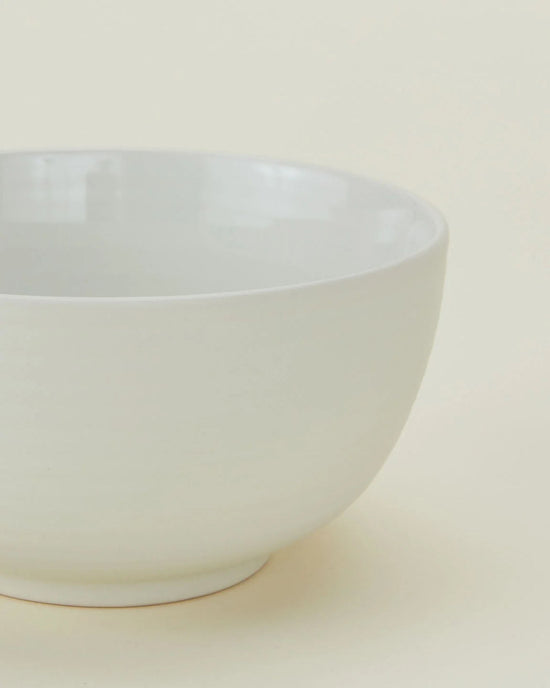 A close-up of a Hawkins New York Essential Large Bowl in Bone, from their stoneware dinnerware set of 4, displayed against a light beige background.