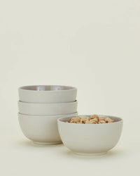 A set of four Essential Large Bowls in Light Grey by Hawkins New York is shown, with three stacked and one filled with square cereal. These stoneware bowls are dishwasher safe and ideal for breakfast or everyday use.