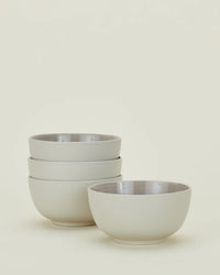Four Essential Large Bowls in Light Grey by Hawkins New York, three stacked on the left and one apart on the right, are displayed against a light background. This set of dishwasher-safe stoneware combines elegance with everyday ease.