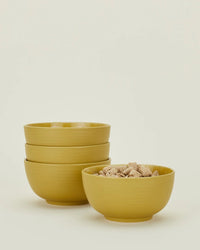 The Essential Large Bowls in Mustard by Hawkins New York, a set of 4, are shown with three stacked and one filled with cereal, presenting a stylish tableware display against a simple light background.