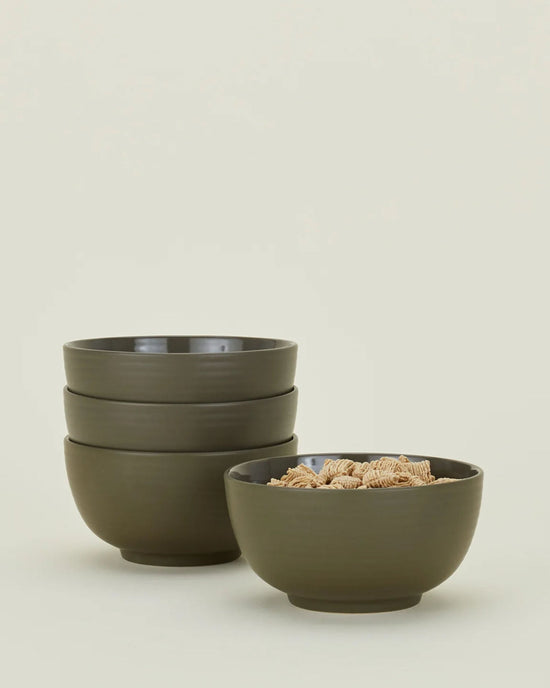Four Essential Large Bowls in Olive by Hawkins New York—three stacked, one filled with square cereal—are displayed on a plain, light backdrop. This stoneware dinnerware set of 4 is dishwasher safe.