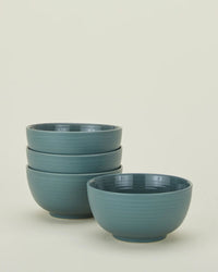 A set of four Essential Large Bowls in Peacock by Hawkins New York, featuring a matte finish, are stacked with three bowls together and one placed separately in front against a plain light background.