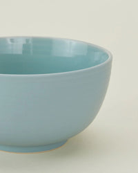 A close-up of the Hawkins New York Essential Large Bowls in Sky—set of 4—shows their glossy light blue finish against an off-white background, making them an elegant, dishwasher safe addition to your dinnerware collection.