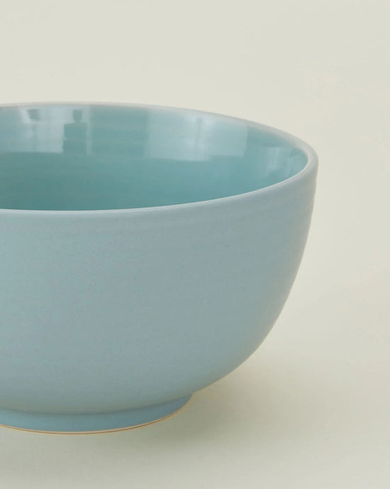 A close-up of the Hawkins New York Essential Large Bowls in Sky—set of 4—shows their glossy light blue finish against an off-white background, making them an elegant, dishwasher safe addition to your dinnerware collection.