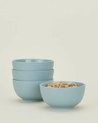 Four Essential Large Bowls in Sky by Hawkins New York—three stacked and one with cereal—are shown against a plain light background; this set of four durable stoneware bowls is dishwasher safe.