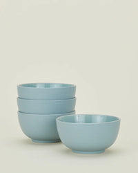 Four Hawkins New York Essential Large Bowls in Sky are shown—three stacked, one in front—on an off-white background. This set of stoneware bowls is durable, dishwasher safe, and perfect for everyday dining.