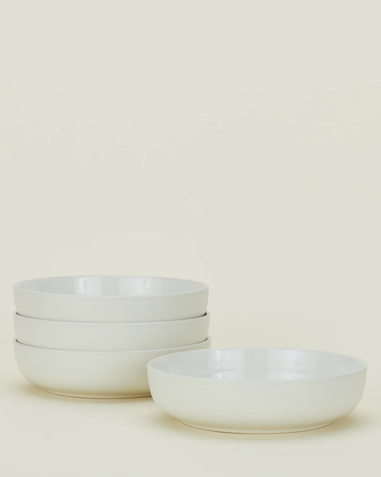 Four Hawkins New York Essential Low Bowls in Bone are displayed on a plain light background—three stacked on the left and one placed separately on the right.
