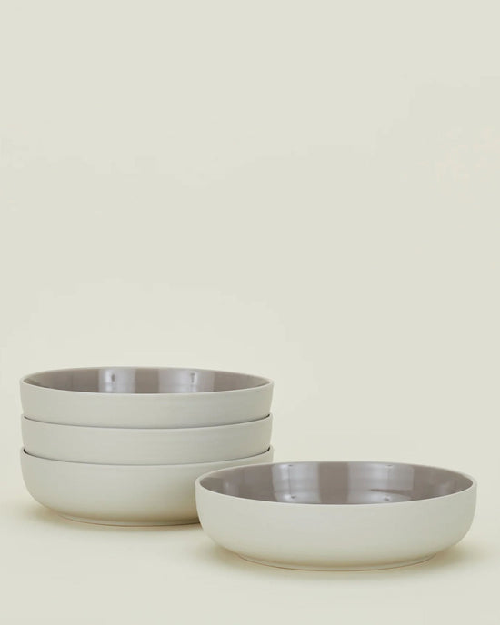 The Essential Low Bowls in Light Grey - Set of 4 by Hawkins New York are stacked in two groups, showing their stoneware construction with glossy interiors and matte exteriors against an off-white background.