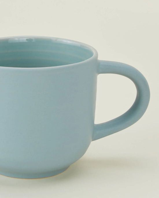 A close-up of a Hawkins New York Essential Mug in Sky, featuring a handle and light blue finish—part of their stoneware Essential Mugs in Sky set of 4.