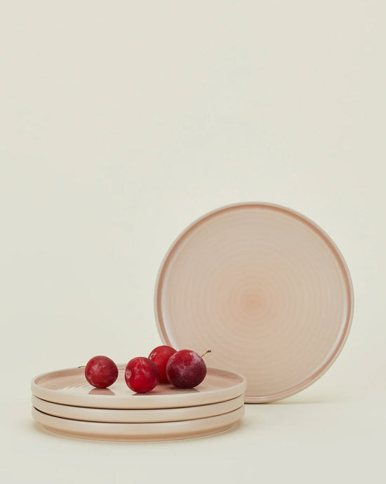 A stack of four Hawkins New York Essential Salad Plates in Blush rests with four red grapes on top, while another matching plate stands upright behind the set against a neutral background.