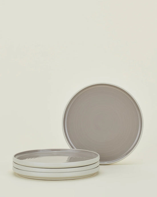 Three stacked Hawkins New York Essential Salad Plates in Light Grey and one upright plate from the set of four are shown against a plain light background. The plates feature a gray color with a white rim.