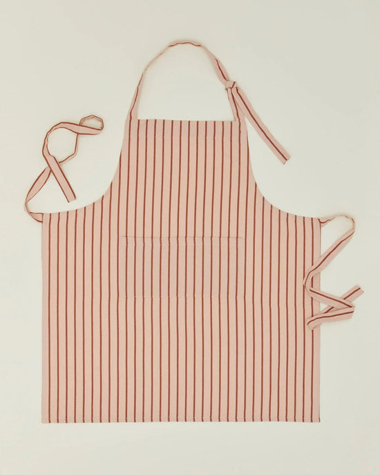 The Hawkins New York Essential Striped Apron in Blush/Terracotta is a cotton apron featuring vertical stripes, an adjustable halter neck loop, two waist ties, and a large central pocket, shown laid flat on a plain background.