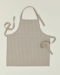 The Hawkins New York Essential Striped Apron in Light Grey/Dark Grey, made of cotton with vertical stripes, includes an adjustable neck strap and waist ties, and is shown laid flat on a light surface.
