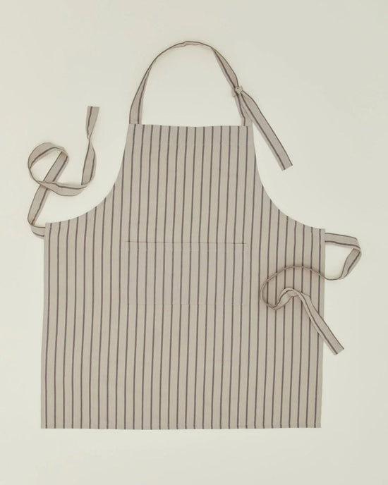 The Hawkins New York Essential Striped Apron in Light Grey/Dark Grey, made of cotton with vertical stripes, includes an adjustable neck strap and waist ties, and is shown laid flat on a light surface.
