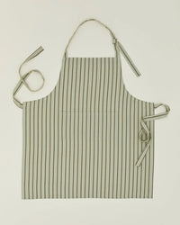 The Hawkins New York Essential Striped Apron in Sage/Olive, made of cotton, features a neck strap, two waist ties, and a front pocket—shown flat on a light background for an effortlessly classic look.