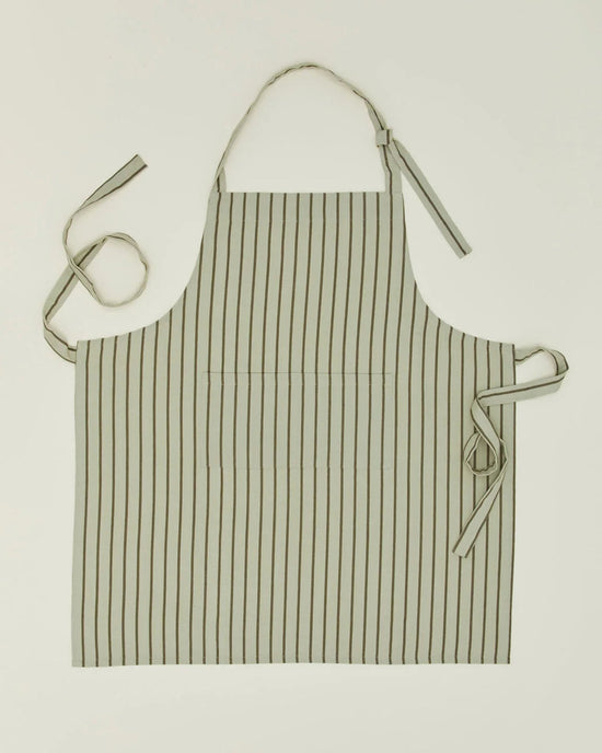 The Hawkins New York Essential Striped Apron in Sage/Olive, made of cotton, features a neck strap, two waist ties, and a front pocket—shown flat on a light background for an effortlessly classic look.