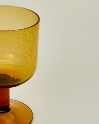 Close-up of a Hawkins New York Set of 4 Stemmed Simple Seeded Glassware in Amber, showcasing the seeded glass with small bubbles, set against a plain light background.