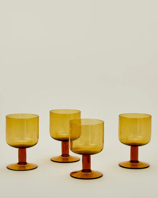 A Set of 4 Stemmed Simple Seeded Glassware in Amber by Hawkins New York is arranged on a neutral surface against a plain background.