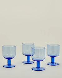 Four Hawkins New York Set of 4 Stemmed Simple Seeded Glassware in Blue are arranged in two rows on a plain, light background, highlighting the timeless elegance of this blue goblet set.