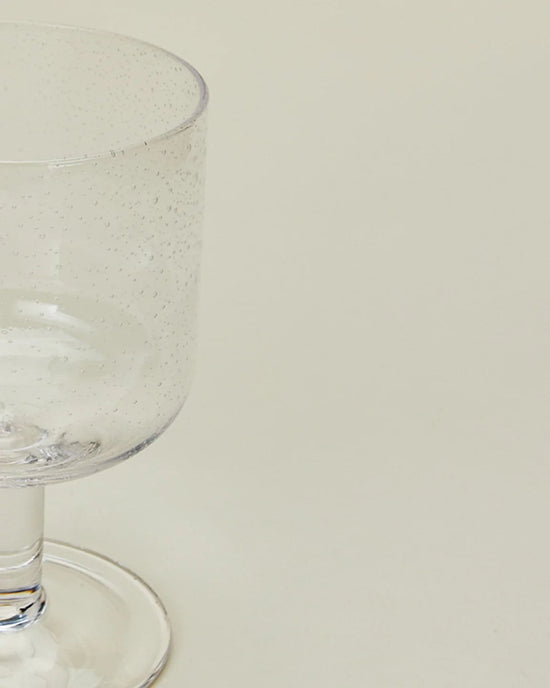 A partially shown Hawkins New York Set of 4 Stemmed Simple Seeded Glassware in Clear, featuring small bubbles, displayed against a plain light background.