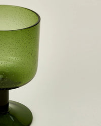 Close-up of an olive Hawkins New York Set of 4 Stemmed Simple Seeded Glassware goblet, featuring textured glass with small bubbles, shown against a plain light background.