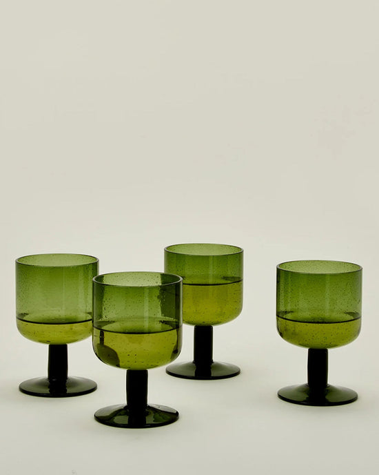 A set of four olive stemmed Simple Seeded Glassware by Hawkins New York is displayed on a plain, light background. Subtle bubbles in the glass evoke classic charm and timeless style.