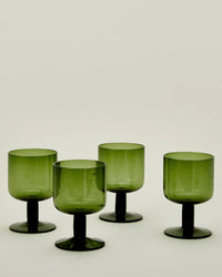 A set of four Hawkins New York Stemmed Simple Seeded Glasses in Olive, featuring short stems and wide bases, is arranged on a plain light-colored background.