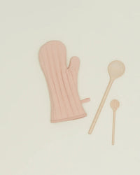 The Simple Linen Oven Mitt in Blush by Hawkins New York sits beside two wooden spoons of varying sizes on a plain light background.