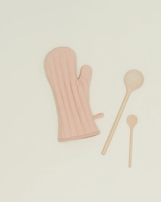 The Simple Linen Oven Mitt in Blush by Hawkins New York sits beside two wooden spoons of varying sizes on a plain light background.