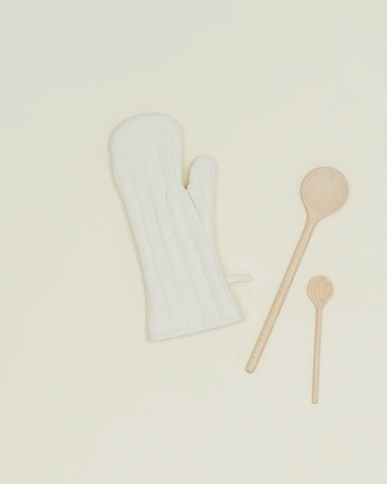 An ivory Simple Linen Oven Mitt by Hawkins New York, featuring heat-resistant padding, is displayed with one large and one small wooden spoon on a plain, light-colored surface.