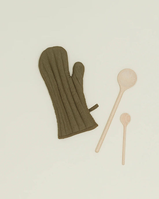 An olive Simple Linen Oven Mitt by Hawkins New York with heat-resistant padding is placed next to a large and a small wooden spoon on a plain light background.