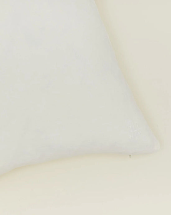 A close-up of the bottom right corner of the Hawkins New York Simple Linen Pillow—18 x 18 inches in ivory with a down insert—set against a light beige background.