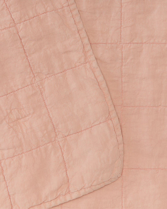 Close-up of the Simple Linen Quilt in Blush by Hawkins New York, featuring a light pink European linen fabric with a grid pattern and stitched details, with one corner of the quilt folded over.