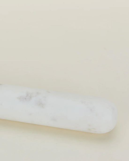 A close-up of the Hawkins New York Simple Marble Rolling Pin, featuring subtle gray veining and set diagonally against a light beige background.