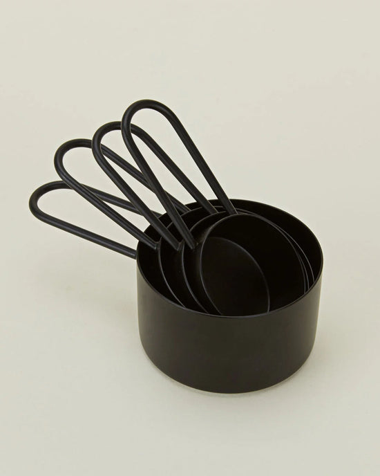 A set of four Hawkins New York Simple Measuring Cups in Black, nested together on a plain light background.