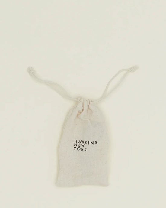A compact, light-colored drawstring pouch with Hawkins New York on the front, ideal for holding your Simple Measuring Spoons in Black, shown against a plain background.