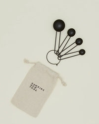 Four Simple Measuring Spoons in Black by Hawkins New York are held on a ring and shown beside a beige drawstring pouch labeled with the brand’s name.