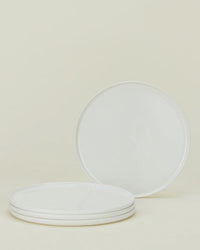 Four round, white plates from the Hawkins New York Simple Porcelain Dinnerware 16 Piece Set are arranged on a neutral background—three stacked and one upright to show its smooth, plain surface.